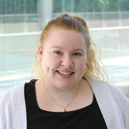 Woman in a white cardigan and black shirt standing in front of windowed background